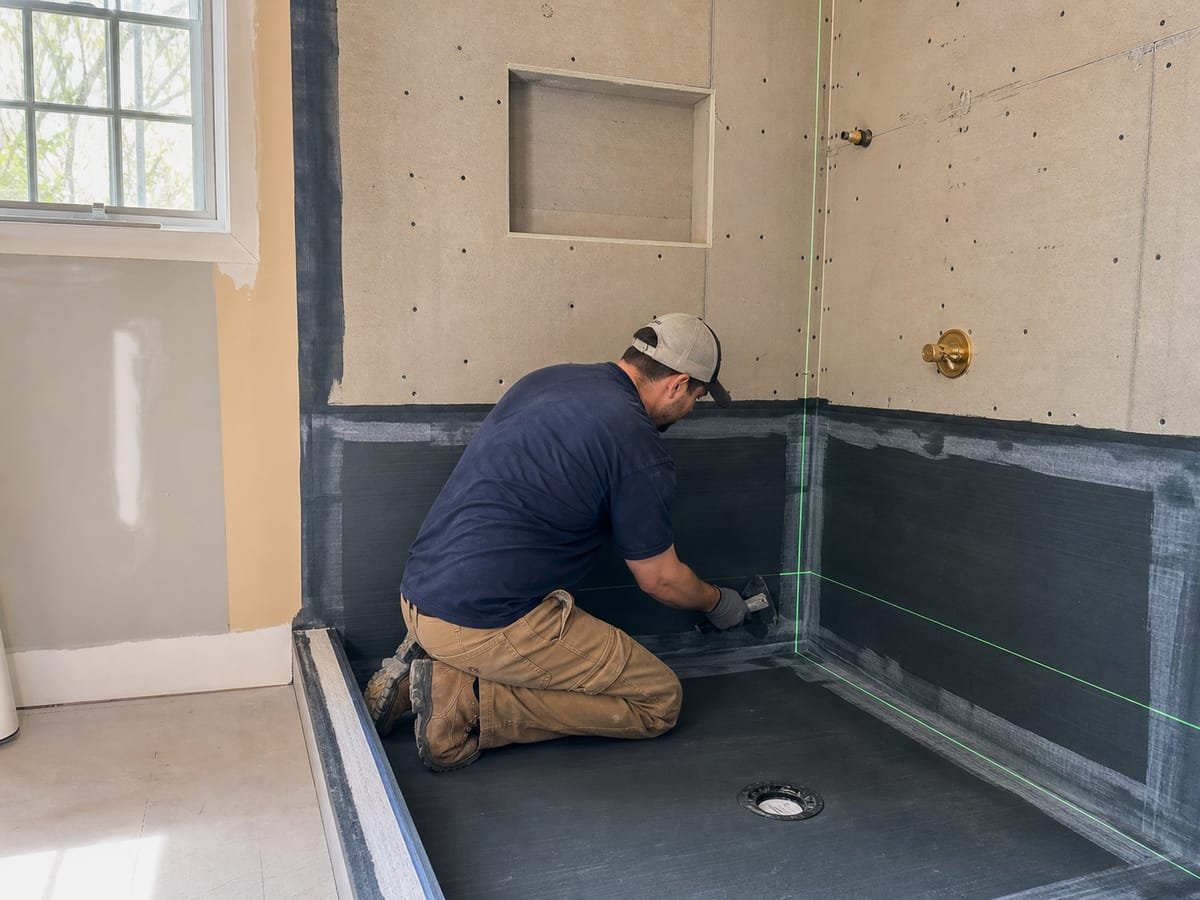Contractor applying waterproofing membrane in a gutted shower