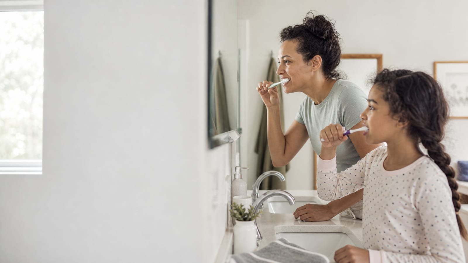 Mother and daughter brushing their teeth together as part of a daily oral health routine